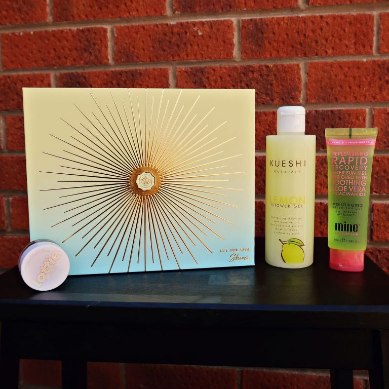 Yellow and blue dual toned Glossybox beauty box with beauty products stood alongside it