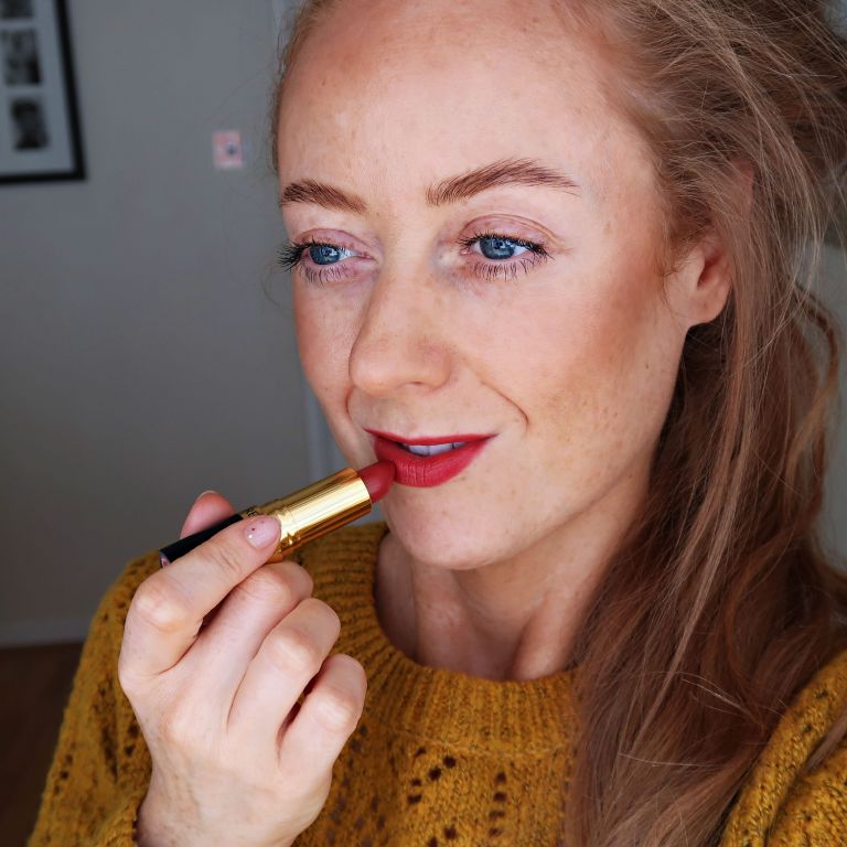 Close up of a girl with ginger hair applying a red Revlon lipstick. Girl in a mustard jumper