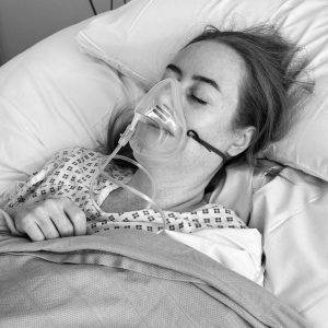 black and white image of a girl laid in hospital bed with nebuliser over her face